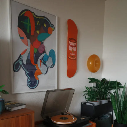 Interior featuring “Colored Campbell's Soup - Peach” by Andy Warhol, highlighting pop art on a vibrant orange skateboard wall piece.