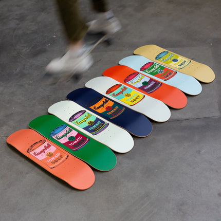 Set of 8 Colored Campbell's Soup skateboards arranged on floor with blurred skater, by Andy Warhol, pop art style.