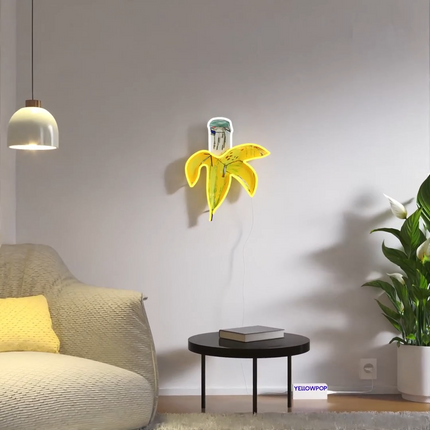 "Banana YP x JM Basquiat" neon artwork displayed on a white wall in a modern living room setting.