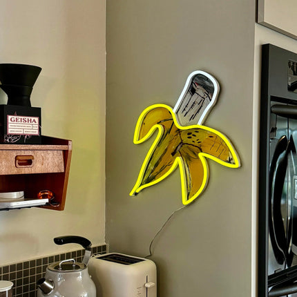 Lifestyle view of "Banana YP x JM Basquiat" neon lamp mounted on a kitchen wall near appliances by Jean-Michel Basquiat