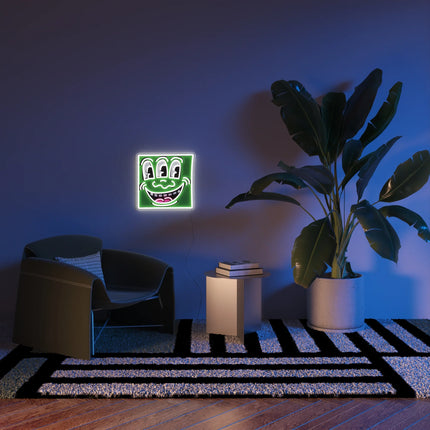 “Triple Eyes YP x Keith Haring” neon lamp artwork displayed in modern living room setting with chair and large plant.
